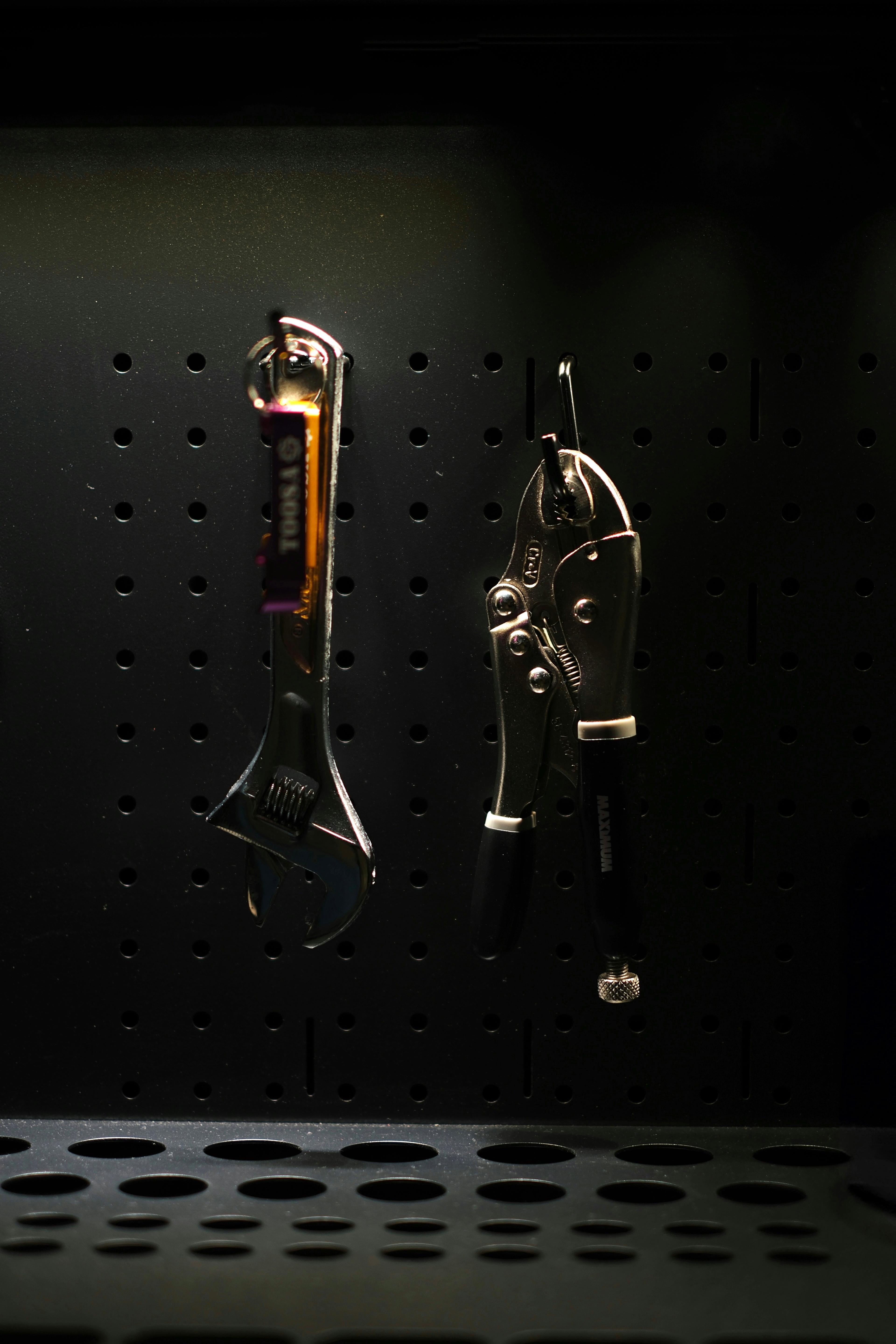 An adjustable wrench and pliers hanging on a pegboard