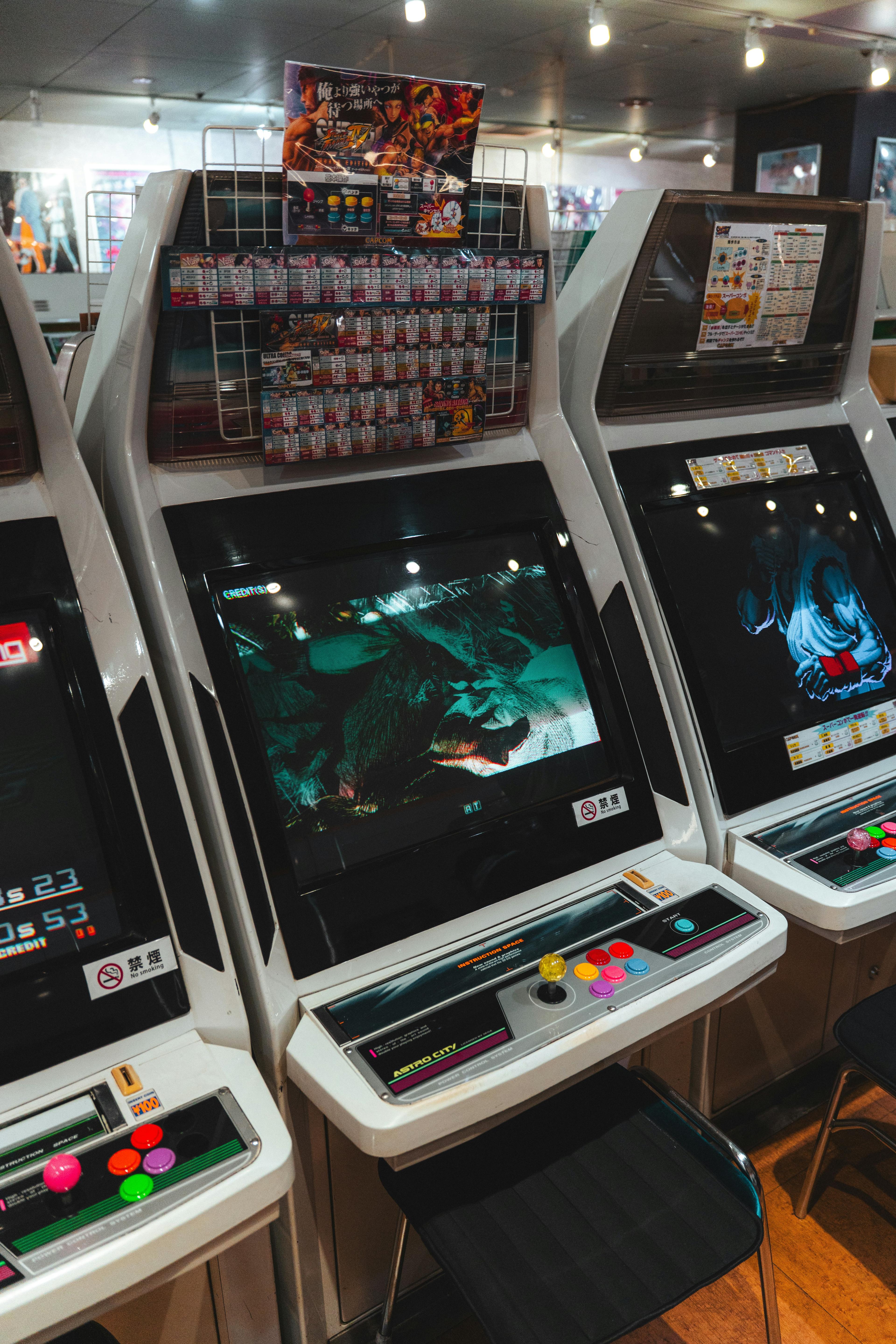 A row of arcade machines with joysticks and lit screens
