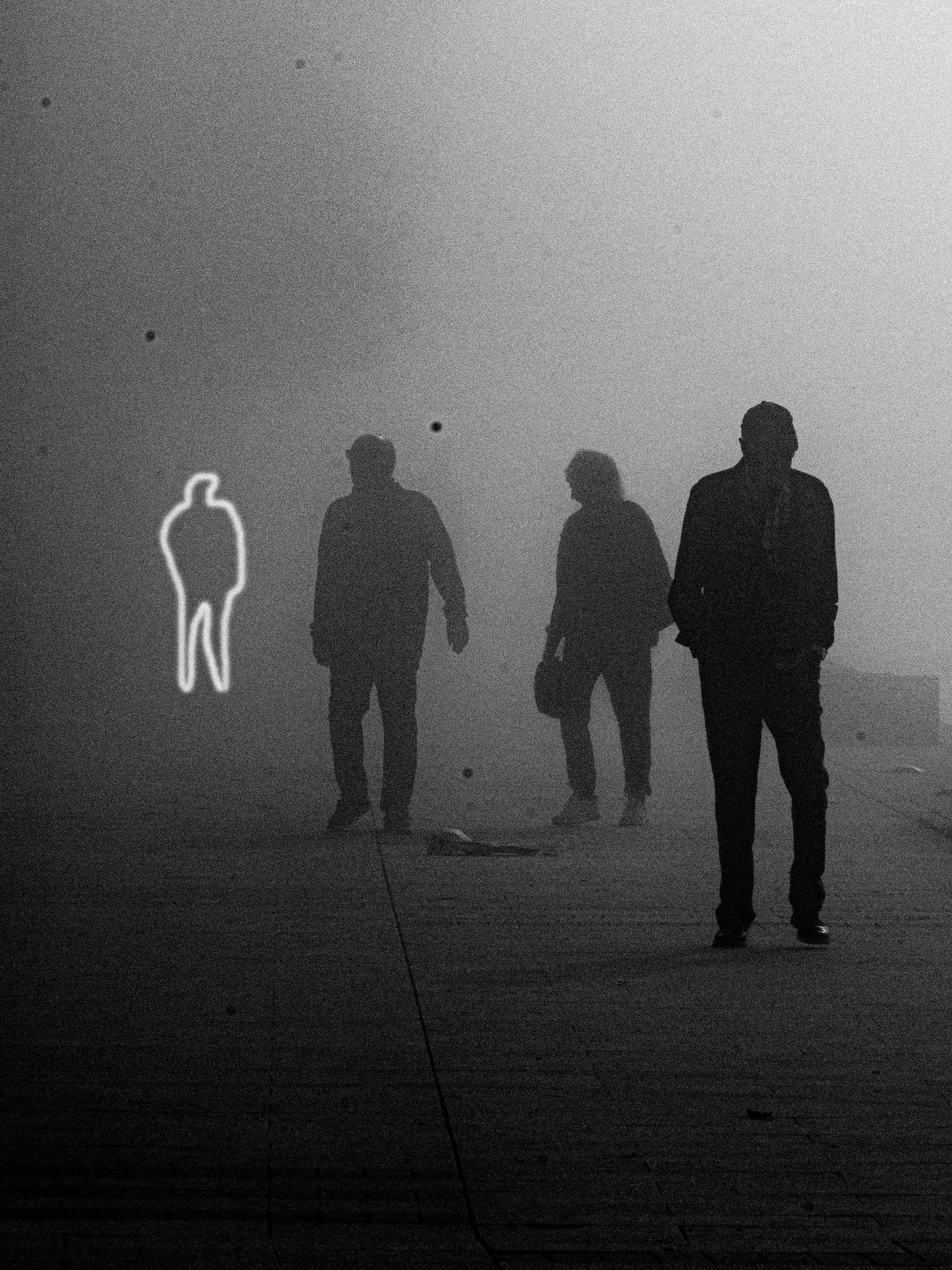 Three silhouetted figures walking in mist beside a glowing outline of a person